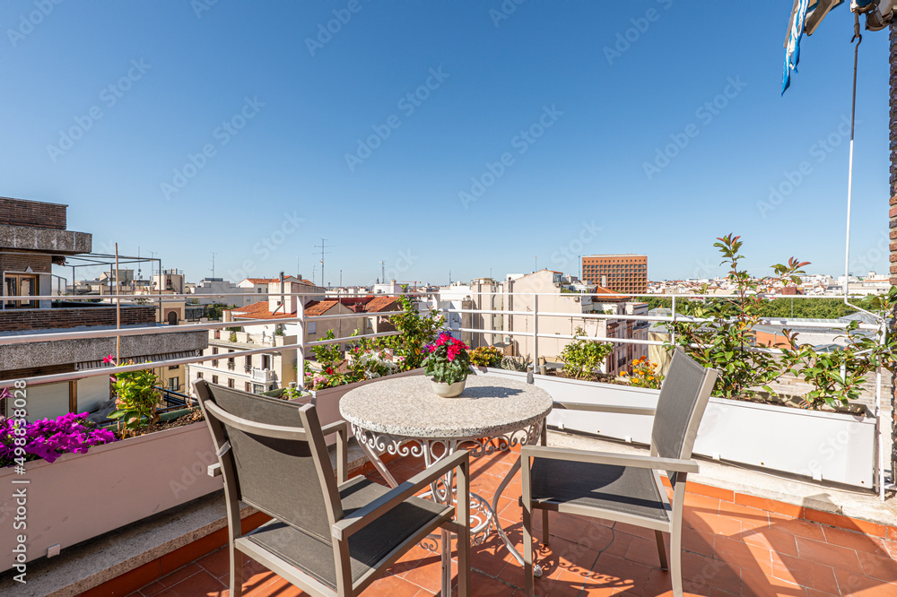 Naklejka premium Nice terrace in a penthouse apartment with lots of flowers, a round stone table and matching chairs with views of the city