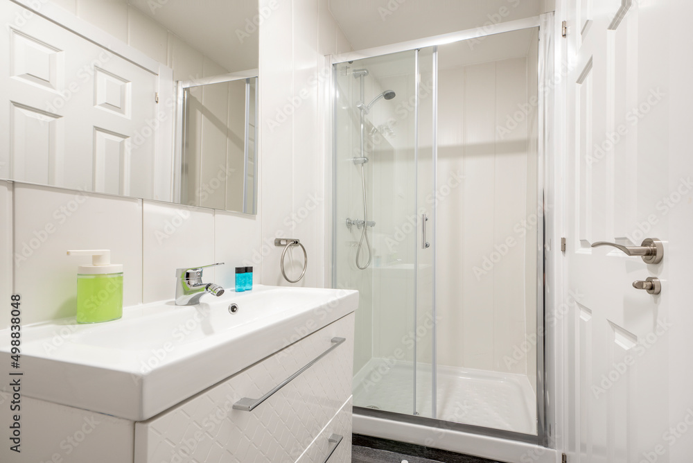 bathroom with one-piece white porcelain sink on lacquered wood cabinet with drawers, wall-mounted frameless square mirror and glass-enclosed shower stall bathroom with one-piece white porcelain sink on lacquered wood cabinet with drawers, wall-mounted frameless square mirror and glass-enclosed shower stall
