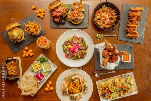 Set of homemade fast food dishes, sandwiches, Mexican al pastor tacos, burgers with fruits, quesadillas and nachos, barbecue wings, chicken fingers and salad with duck confit © Toyakisfoto.photos