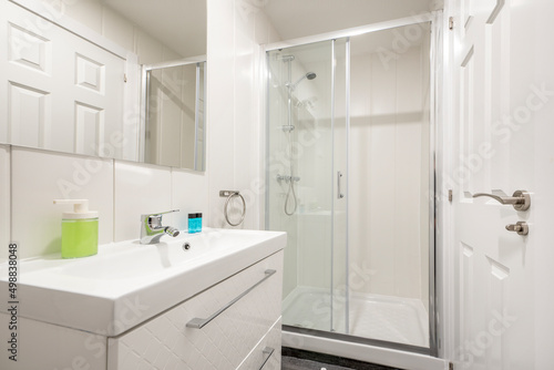bathroom with one-piece white porcelain sink on lacquered wood cabinet with drawers, wall-mounted frameless square mirror and glass-enclosed shower stall