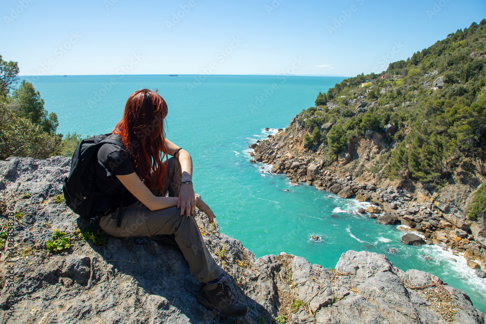 Woman trekker sits on the top of the mountain above the sea