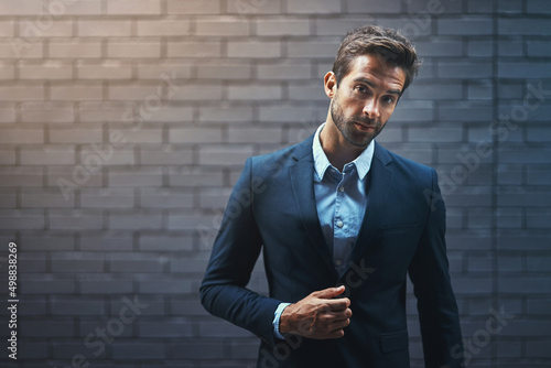 Dress for success and then go out and get it. Portrait of a handsome young businessman standing against a grey facebrick wall. photo