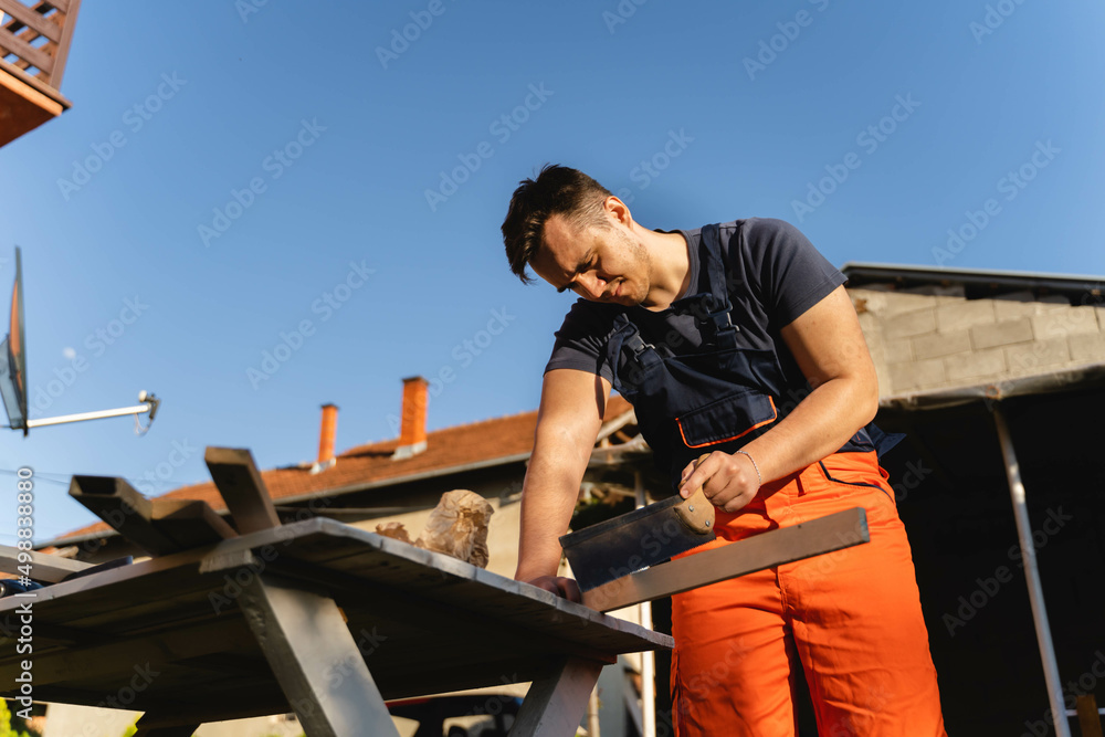 A man is using handsaw on a piece of wood on his workbench in backyard during the day A man is using handsaw on a piece of wood on his workbench in backyard during the day
