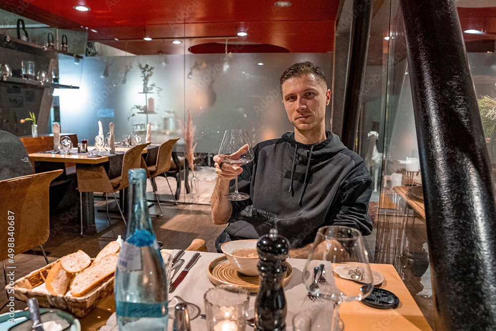 St. Anton am Arlberg. March 10, 2022. Young man holding champagne glass beside elegant table setting in restaurant, Handsome man hold drink glass by table served with food in hotel
