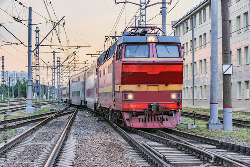 Passenger retro electric czech locomotive with train departs from the station at sunset time.