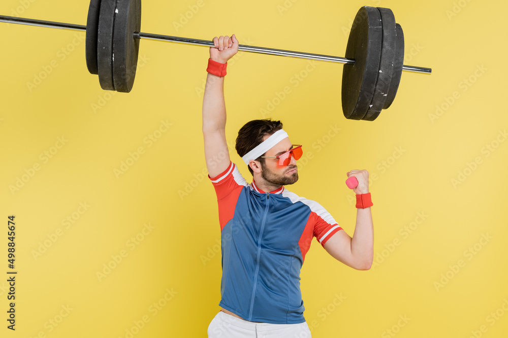 Obraz premium Sportsman lifting barbell and dumbbell isolated on yellow.