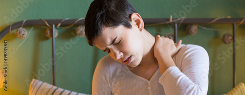 Young woman having neck pains sitting on the bed in bedroom at home photo