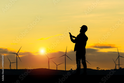 Silhouette of Engineer man checking project at wind farm site on sunset in evening time