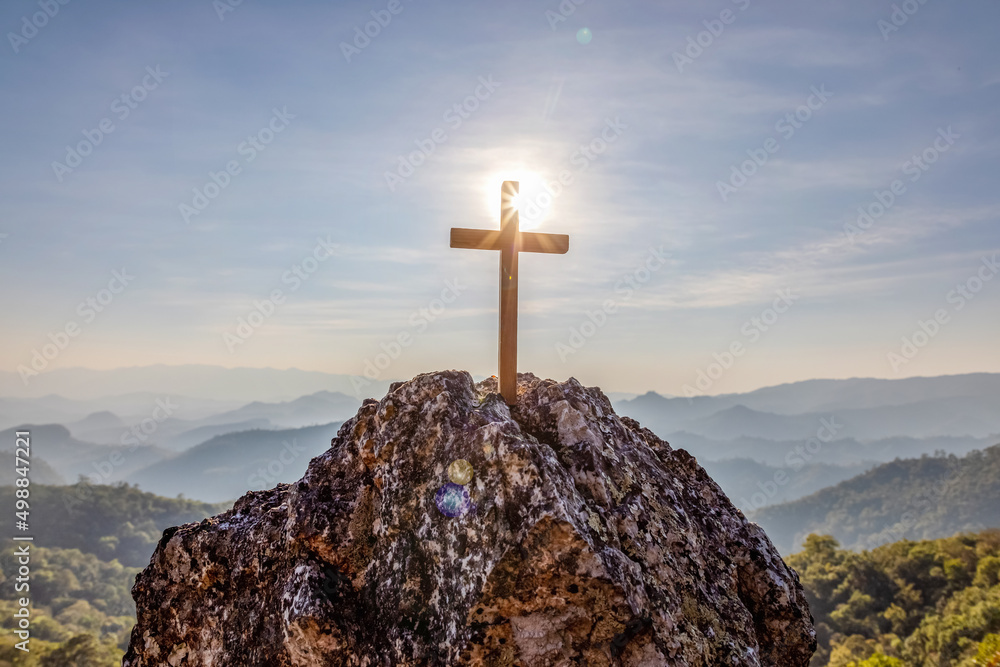 Silhouettes of crucifix symbol on top mountain with bright sunbeam on the colorful sky background Silhouettes of crucifix symbol on top mountain with bright sunbeam on the colorful sky background