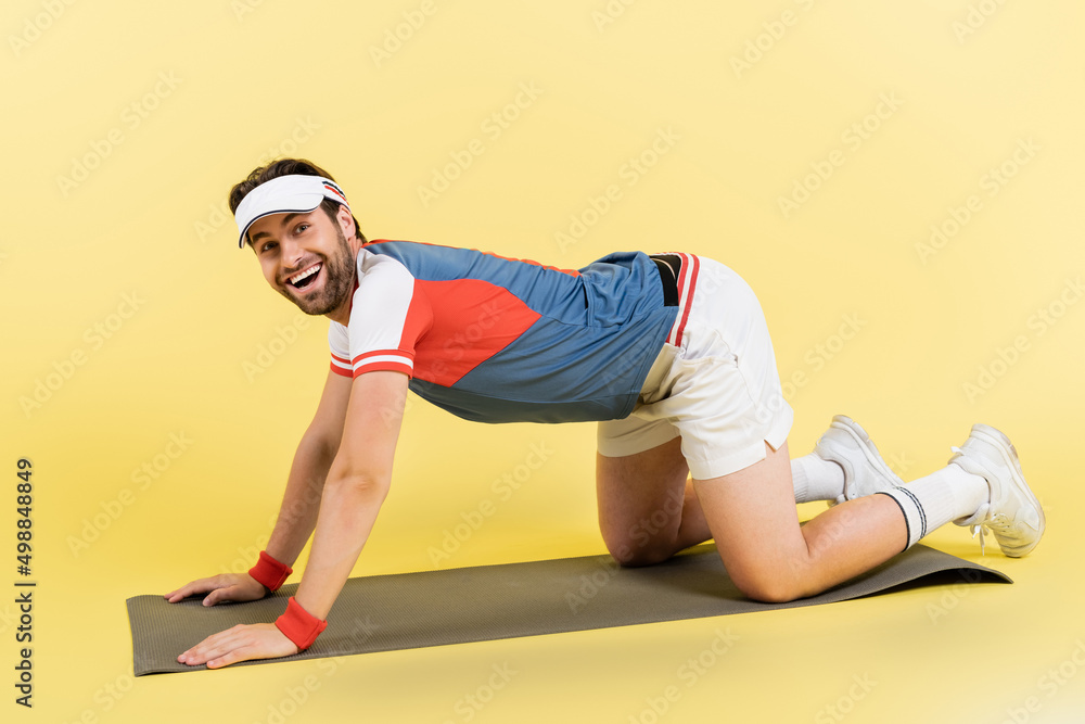 Naklejka premium Positive sportsman standing on fitness mat on yellow background.