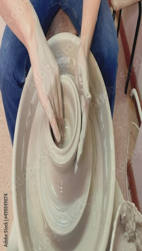 a man in a white t-shirt and jeans in a pottery workshop works with clay, on a potter's wheel. close-up hands in clay. craftsman at hand work.  photo