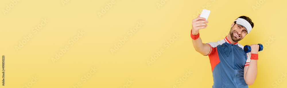 Happy sportsman taking selfie and training with dumbbell isolated on yellow, banner. Happy sportsman taking selfie and training with dumbbell isolated on yellow, banner.