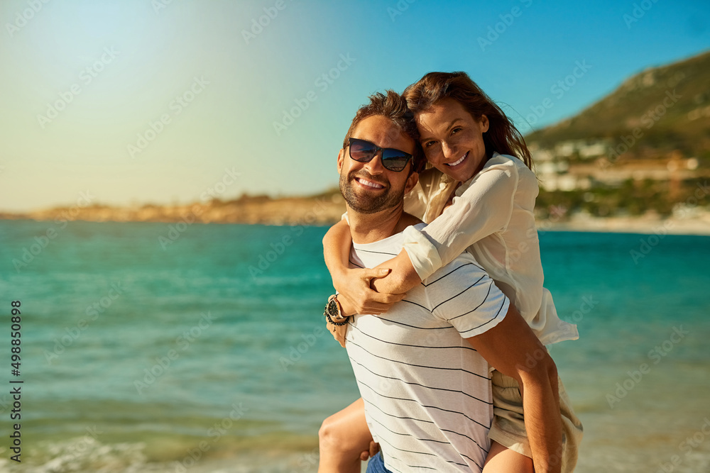 The perfect day for some fun and romance. Shot of a happy young couple  enjoying a piggyback ride at the beach. Stock Photo | Adobe Stock