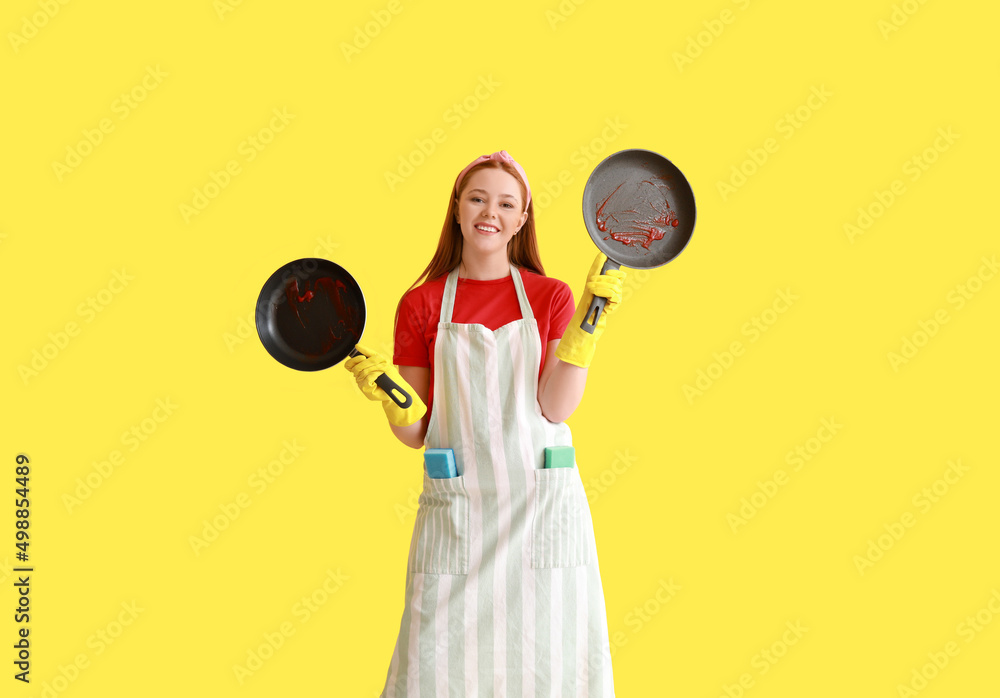 Young woman with dirty frying pans on color background Young woman with dirty frying pans on color background