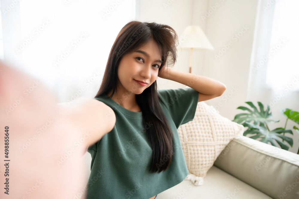 Pretty young asian female with big smile sitting at living room. She having fun taking light cheerful selfie on blurred background Pretty young asian female with big smile sitting at living room. She having fun taking light cheerful selfie on blurred background