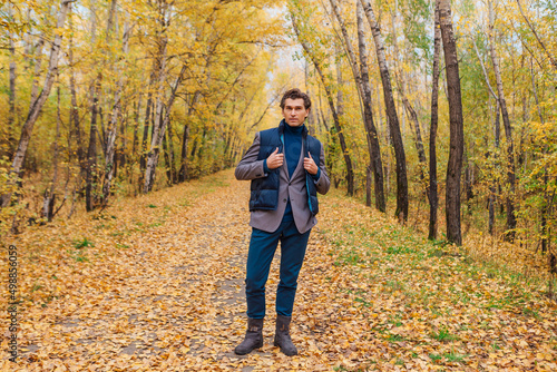 Tall handsome man dressed in a brown jacket walking in the autumn alley © Smile