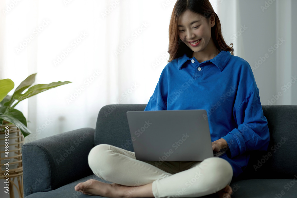 Young business freelance Asian woman working on laptop checking social media while lying on the sofa when relax in living room at home. Young business freelance Asian woman working on laptop checking social media while lying on the sofa when relax in living room at home.
