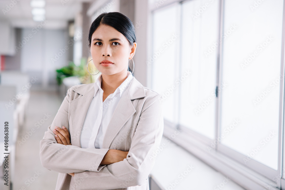 A young businesswoman stands and looks at the camera with a confident expression in the office. A young businesswoman stands and looks at the camera with a confident expression in the office.