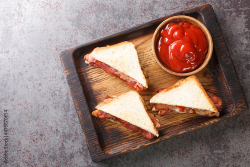 Sandwich with crispy bacon melted butter and ketchup close-up on a wooden tray on the table. horizontal top view from above photo