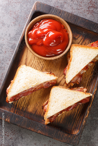 Bacon Butty  sandwich of fried bacon between bread that is optionally spread with butter, and may be seasoned with ketchup closeup in the wooden tray on the table. Vertical top view from above photo