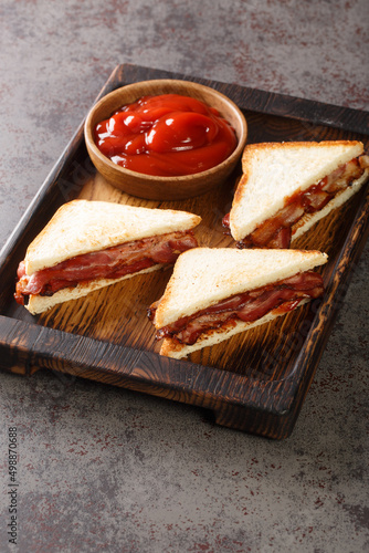 Bacon Butty  sandwich of fried bacon between bread that is optionally spread with butter, and may be seasoned with ketchup closeup in the wooden tray on the table. Vertical photo