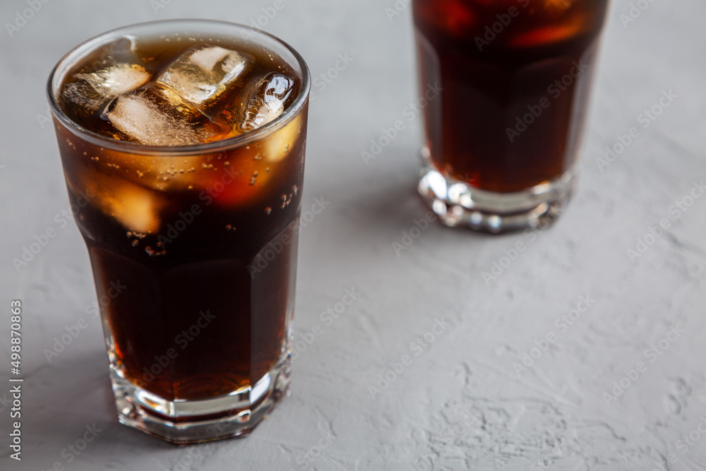 Cold Refreshing Dark Cola with Ice Cubes, Straws on a gray surface, side view. Cold Refreshing Dark Cola with Ice Cubes, Straws on a gray surface, side view.