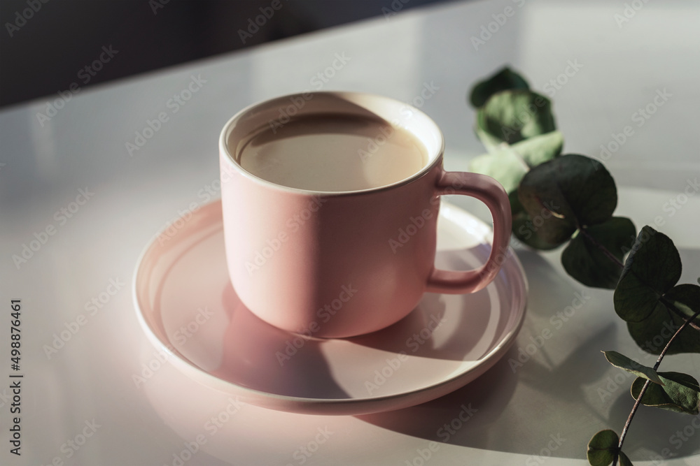 Cup of coffee on a white table and eucalyptus branch with hard shadows Cup of coffee on a white table and eucalyptus branch with hard shadows
