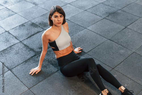 Sitting on the ground. Woman in sportive clothes with slim body type is in the gym