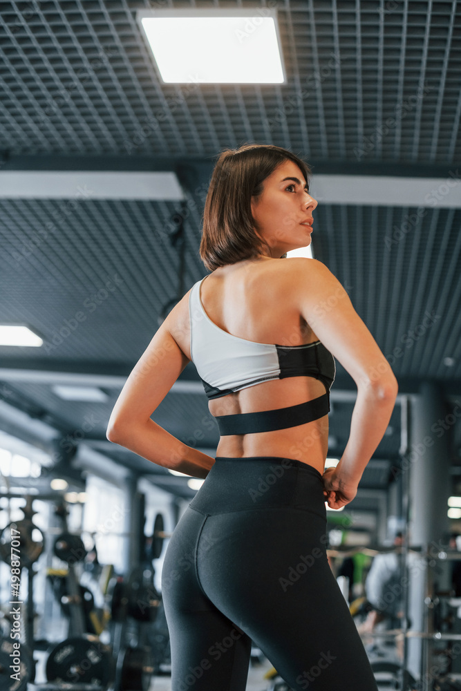 Side view. Woman in sportive clothes with slim body type is in the gym Side view. Woman in sportive clothes with slim body type is in the gym