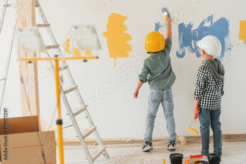 Rear view. Two boys painting walls in the domestic room