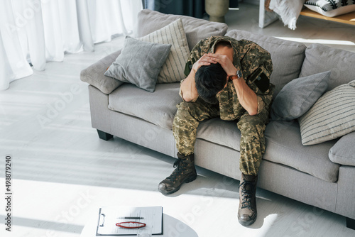 Bad mood. Post traumatic stress disorder. Soldier in uniform sitting indoors photo