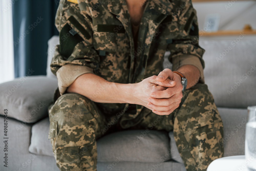 Close up view. Soldier in uniform is indoors in the domestic room Close up view. Soldier in uniform is indoors in the domestic room