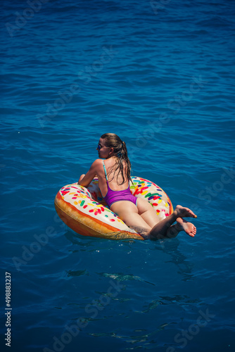 Beautiful young woman in the sea swims on an inflatable ring and has fun on vacation. Girl in a bright swimsuit at the sea under the sunlight © Дмитрий Ткачук