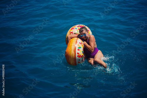 Beautiful young woman fell from an inflatable circle into the blue sea. Girl on vacation swims with a circle on the sea