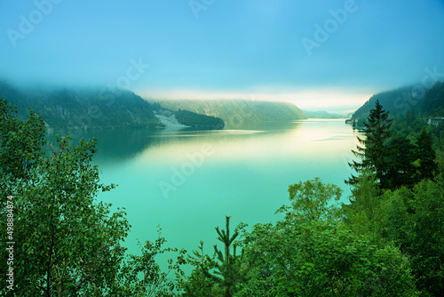 interesting morning mood, turquoise lake Achensee, clouds above and light spot from clearing fog