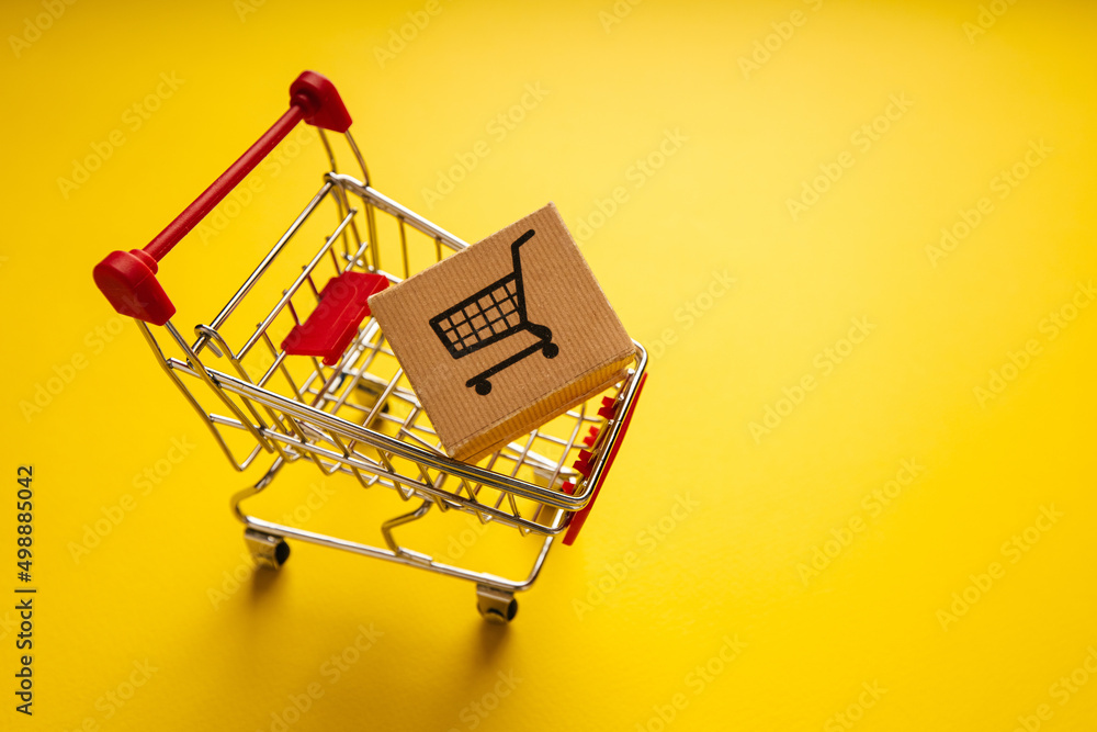 Shopping cart and delivery box on yellow background with copy space. Shopping and delivery concept Shopping cart and delivery box on yellow background with copy space. Shopping and delivery concept