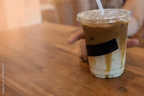 Iced coffee in a plastic cup, ready to serve on a brown wooden table. while someone's hand was picking up to drink To add happiness in the afternoon