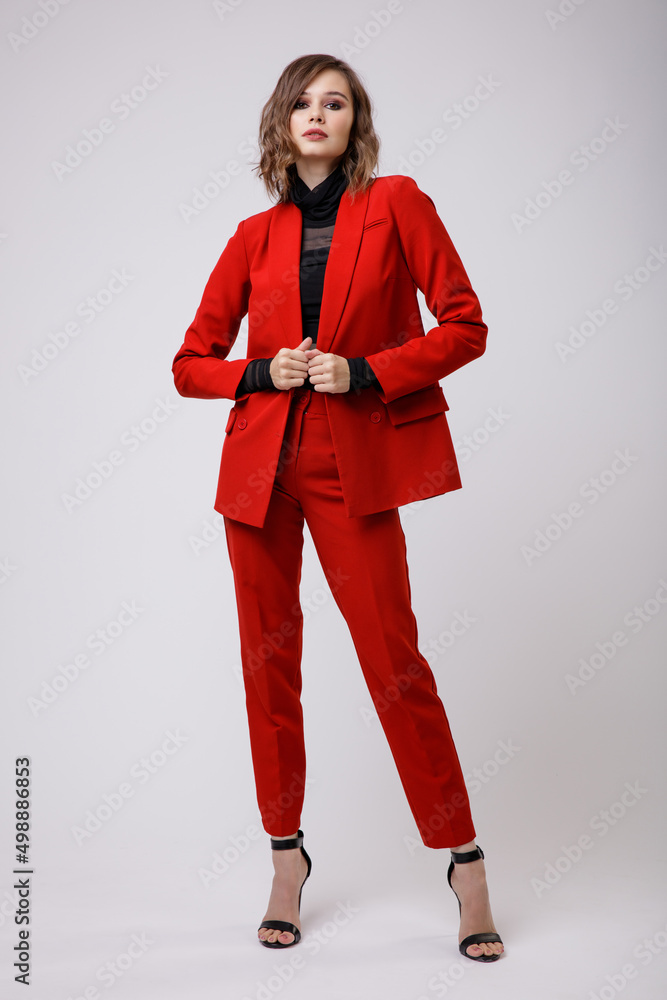 High fashion photo of a beautiful elegant young woman in a pretty red suit, jacket, pants, trousers, black blouse posing on white background. Slim figure, hairstyle, studio shot High fashion photo of a beautiful elegant young woman in a pretty red suit, jacket, pants, trousers, black blouse posing on white background. Slim figure, hairstyle, studio shot