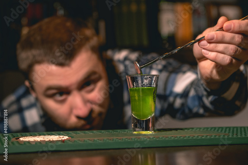 Bartender taking out bar spoon from shot glass with green drink