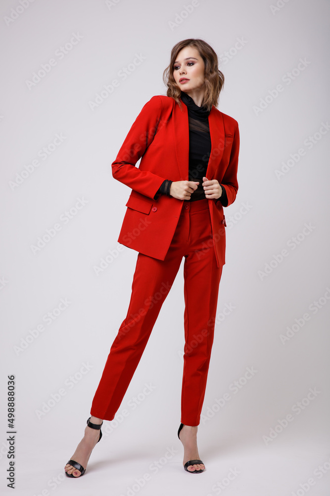 High fashion photo of a beautiful elegant young woman in a pretty red suit, jacket, pants, trousers, black blouse posing on white background. Slim figure, hairstyle, studio shot High fashion photo of a beautiful elegant young woman in a pretty red suit, jacket, pants, trousers, black blouse posing on white background. Slim figure, hairstyle, studio shot
