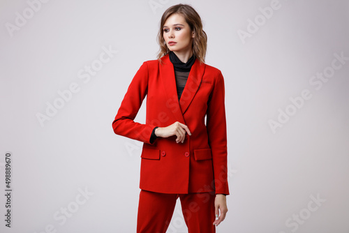 High fashion photo of a beautiful elegant young woman in a pretty red suit, jacket, pants, trousers, black blouse posing on white background. Slim figure, hairstyle, studio shot