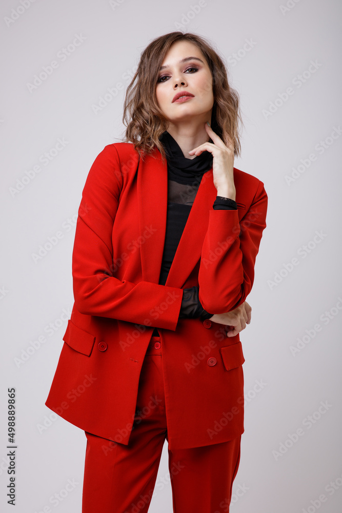 High fashion photo of a beautiful elegant young woman in a pretty red suit, jacket, pants, trousers, black blouse posing on white background. Slim figure, hairstyle, studio shot High fashion photo of a beautiful elegant young woman in a pretty red suit, jacket, pants, trousers, black blouse posing on white background. Slim figure, hairstyle, studio shot