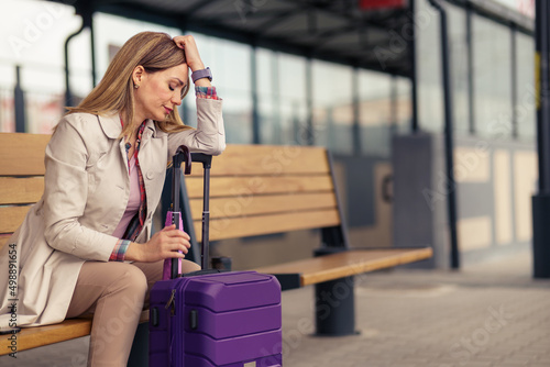 A beautiful woman sits leaning on a suitcase at a train station. She's tired and has a headache.