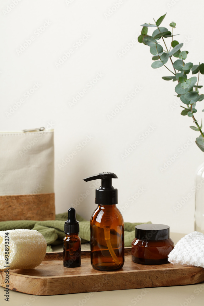 Brown amber glass cosmetic bottles on wooden tray on table with cosmetic bag and eucalyptus. Luxury SPA bathroom beauty products set.