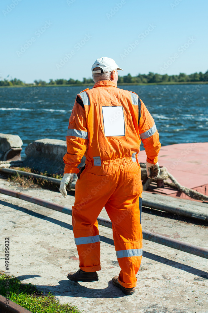 a docker man walks along the pier against the background of a moored barge