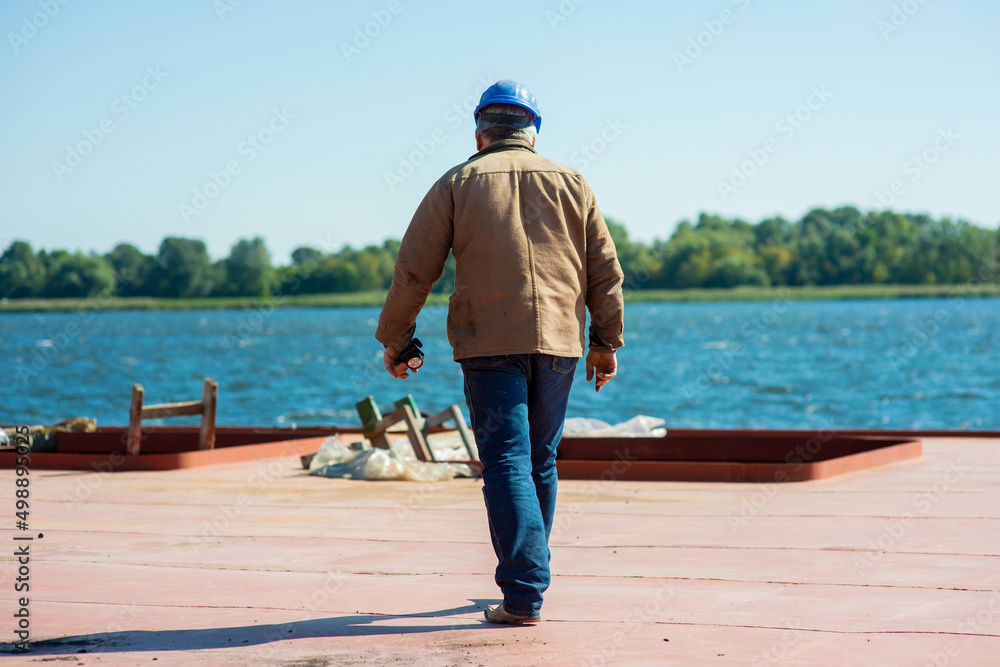 a male docker in a helmet walks along the deck of a river barge moored in the port a male docker in a helmet walks along the deck of a river barge moored in the port