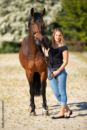 Full length shot of a young woman with a horse in the sunshine at the riding arena..