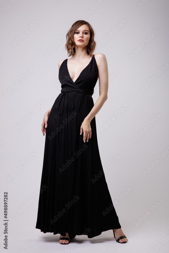 High fashion photo of a beautiful elegant young woman in a pretty black evening party dress with a deep neckline posing on white background. Slim figure, hairstyle, studio shot. High fashion photo of a beautiful elegant young woman in a pretty black evening party dress with a deep neckline posing on white background. Slim figure, hairstyle, studio shot.