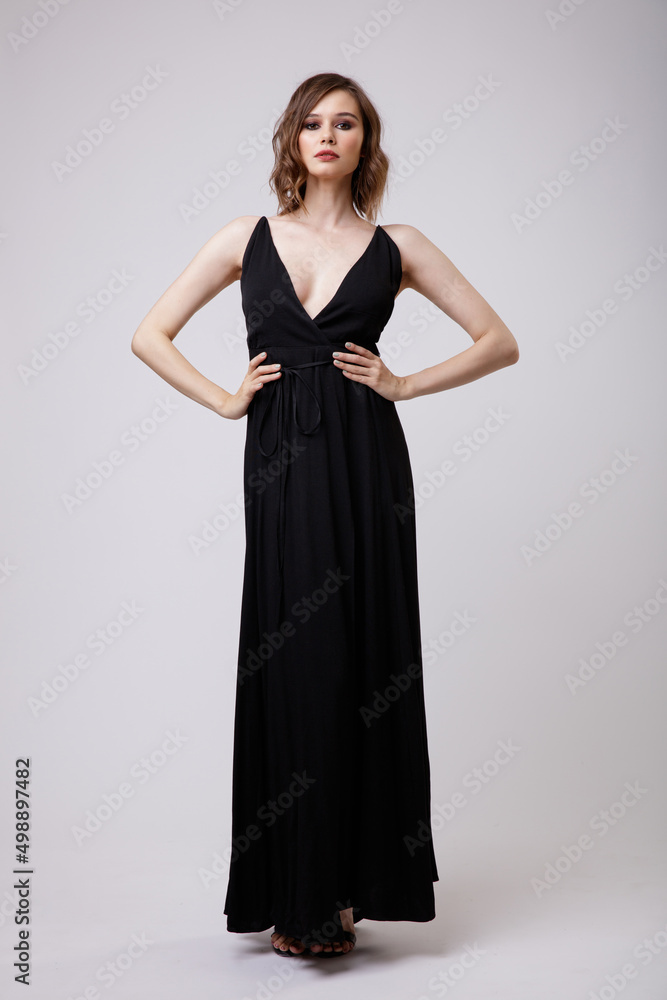 High fashion photo of a beautiful elegant young woman in a pretty black evening party dress with a deep neckline posing on white background. Slim figure, hairstyle, studio shot. High fashion photo of a beautiful elegant young woman in a pretty black evening party dress with a deep neckline posing on white background. Slim figure, hairstyle, studio shot.