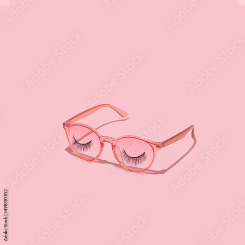 Creative layout with pink eyeglasses and false eyelashes on pastel pink background. 80s or 90s retro fashion aesthetic concept. Minimal romantic makeup idea.
